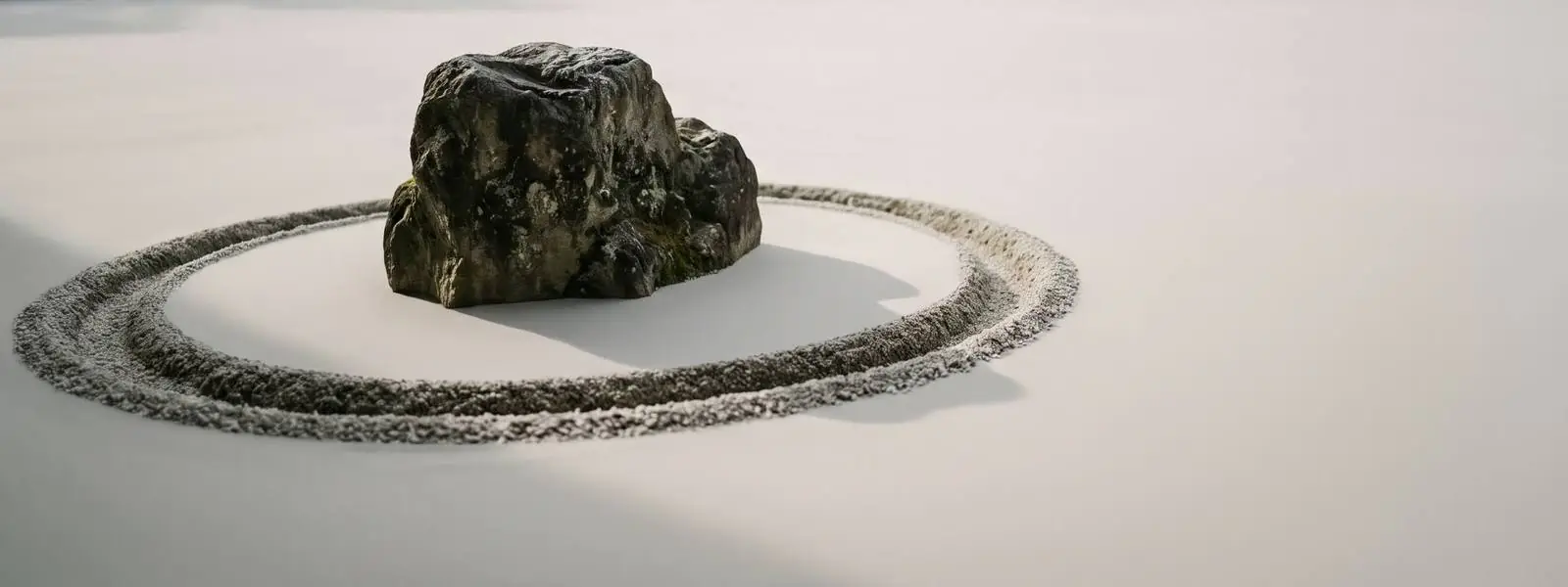 A single stone in a smooth bed of pale gravel with one freshly raked ring drawn around it