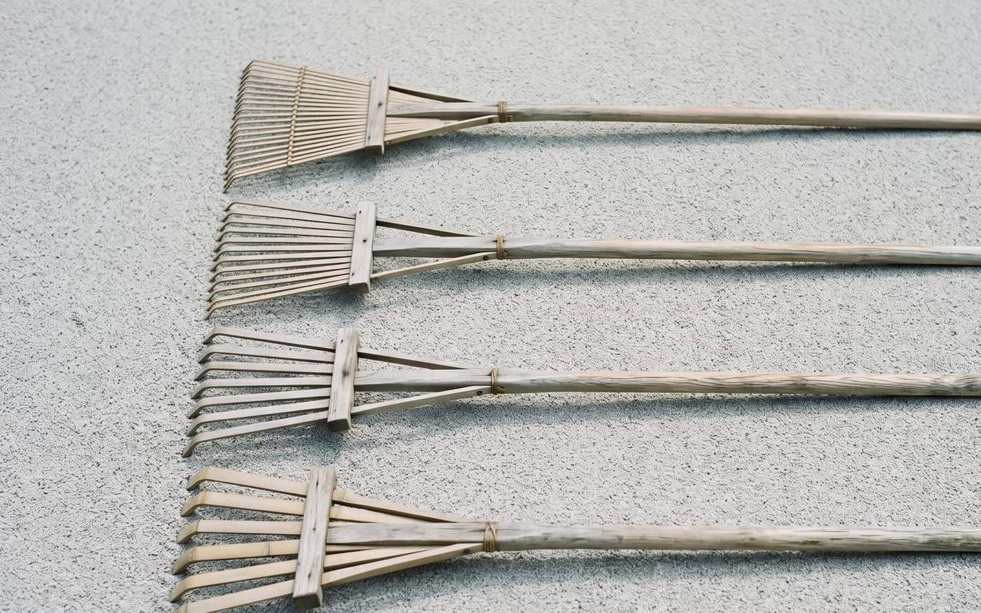 Four traditional wooden Japanese garden rakes laid out in parallel on gravel, each with a different tine width