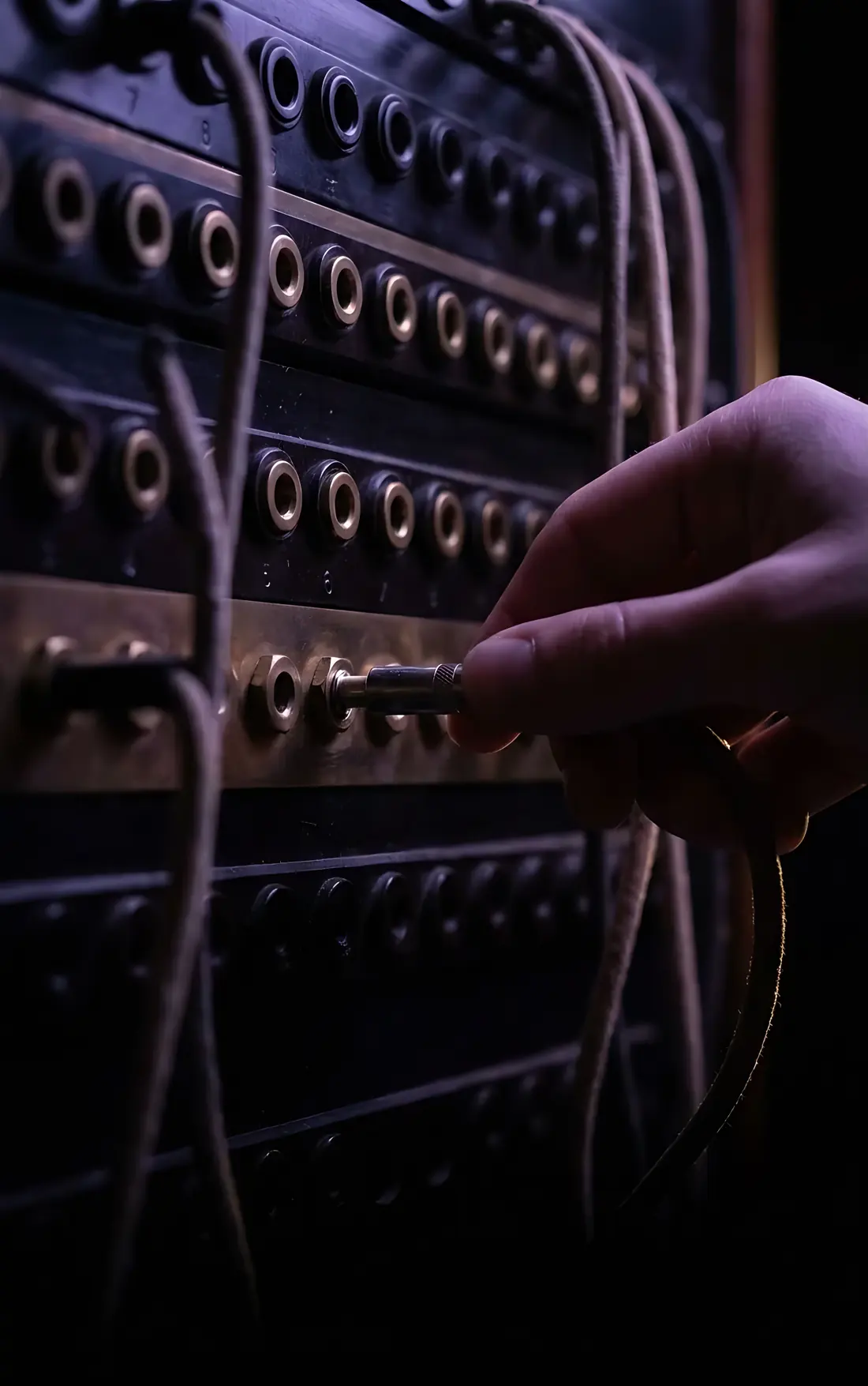 A hand plugging a patch cord into one socket of a vintage telephone switchboard