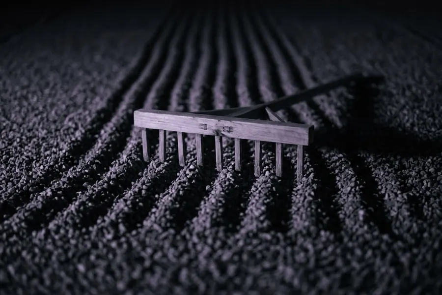 A wooden rake resting in raked gravel at night